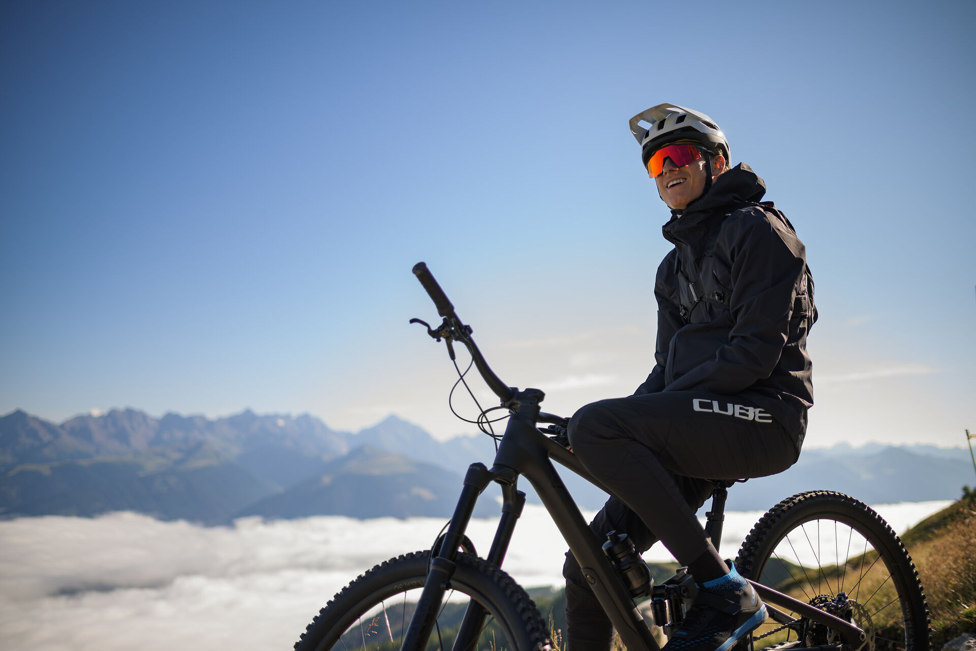 Radfahrer auf einem Gipfel über dem Wolkenmeer mit Blick auf die Alpen